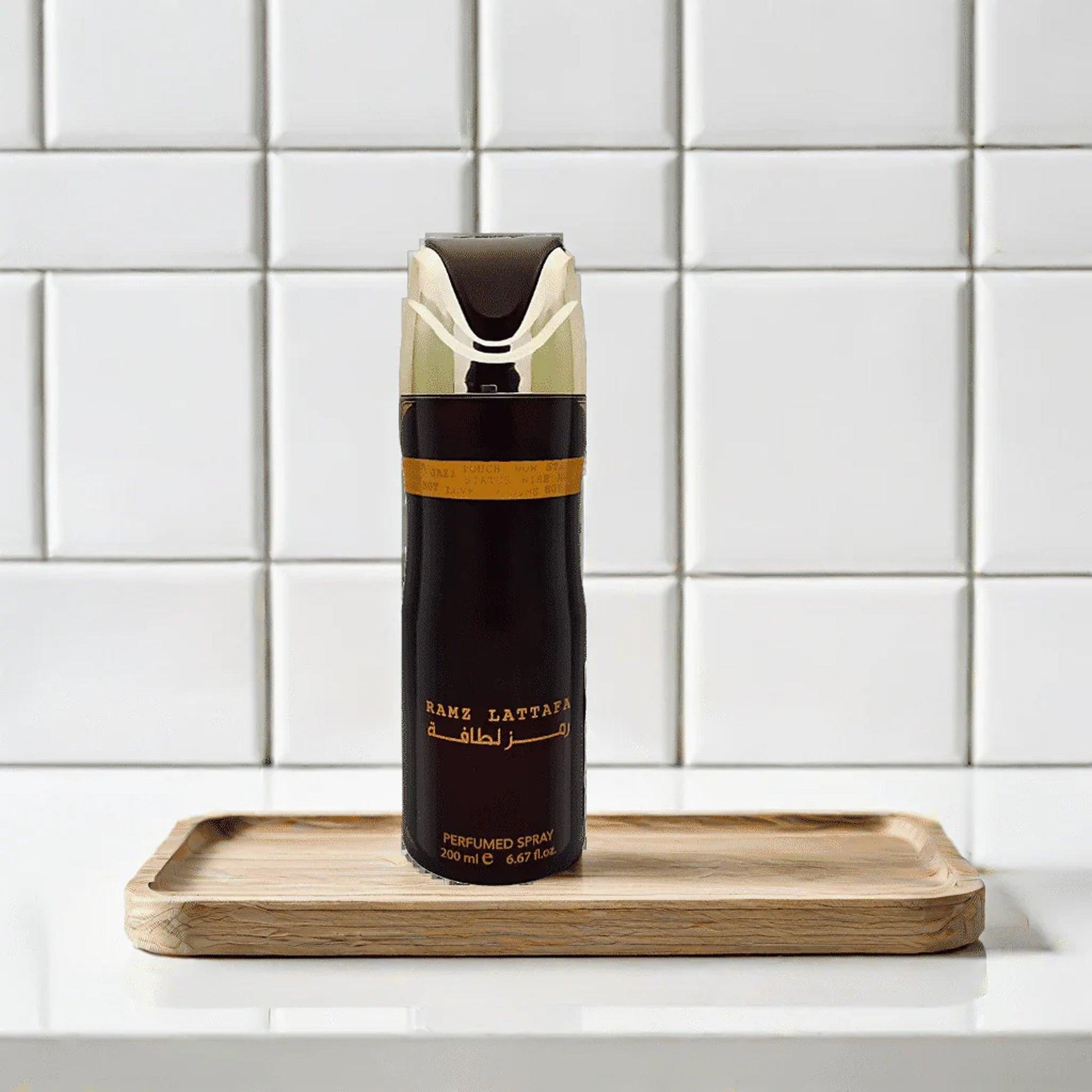 Lattafa Ramz Lattafa perfumed spray bottle in black and gold placed on a wooden tray against a white tiled background