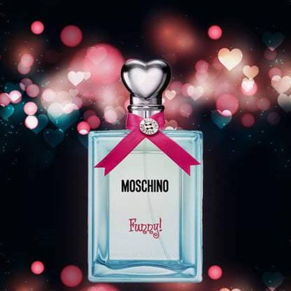 Moschino Funny Eau De Toilette bottle with a silver heart-shaped cap and pink ribbon, set against a dark background with glowing bokeh heart lights