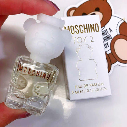 Moschino Toy 2 Eau De Parfum mini bottle shaped like a clear glass teddy bear held by hand beside its white and gold packaging box