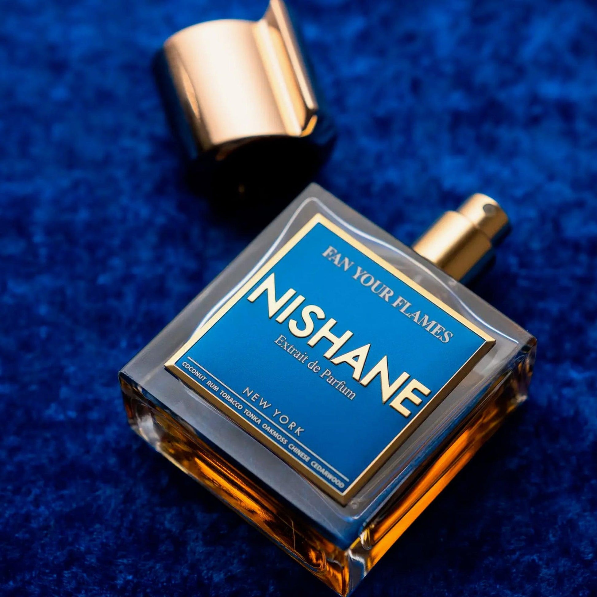 Nishane Fan Your Flames Extrait de Parfum bottle with golden cap placed on a deep blue textured surface, showcasing its elegant blue and gold design
