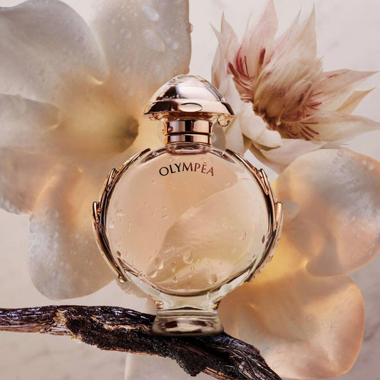 Paco Rabanne Olympea Eau De Parfum round gold-accented bottle with water droplets placed on a branch against a soft floral background