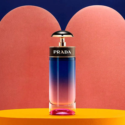 Prada Candy Night Eau De Parfum bottle with gradient pink-to-blue design placed on an orange surface against a pink and navy abstract background