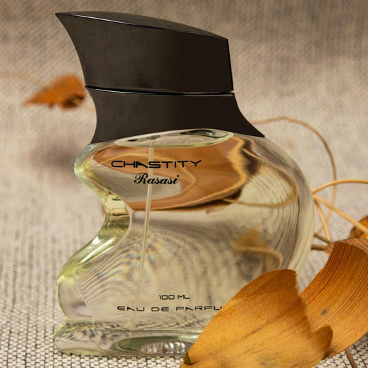 Rasasi Chastity Eau De Parfum 100ml perfume bottle with a sculpted glass design placed on a textured beige surface surrounded by dried autumn leaves.