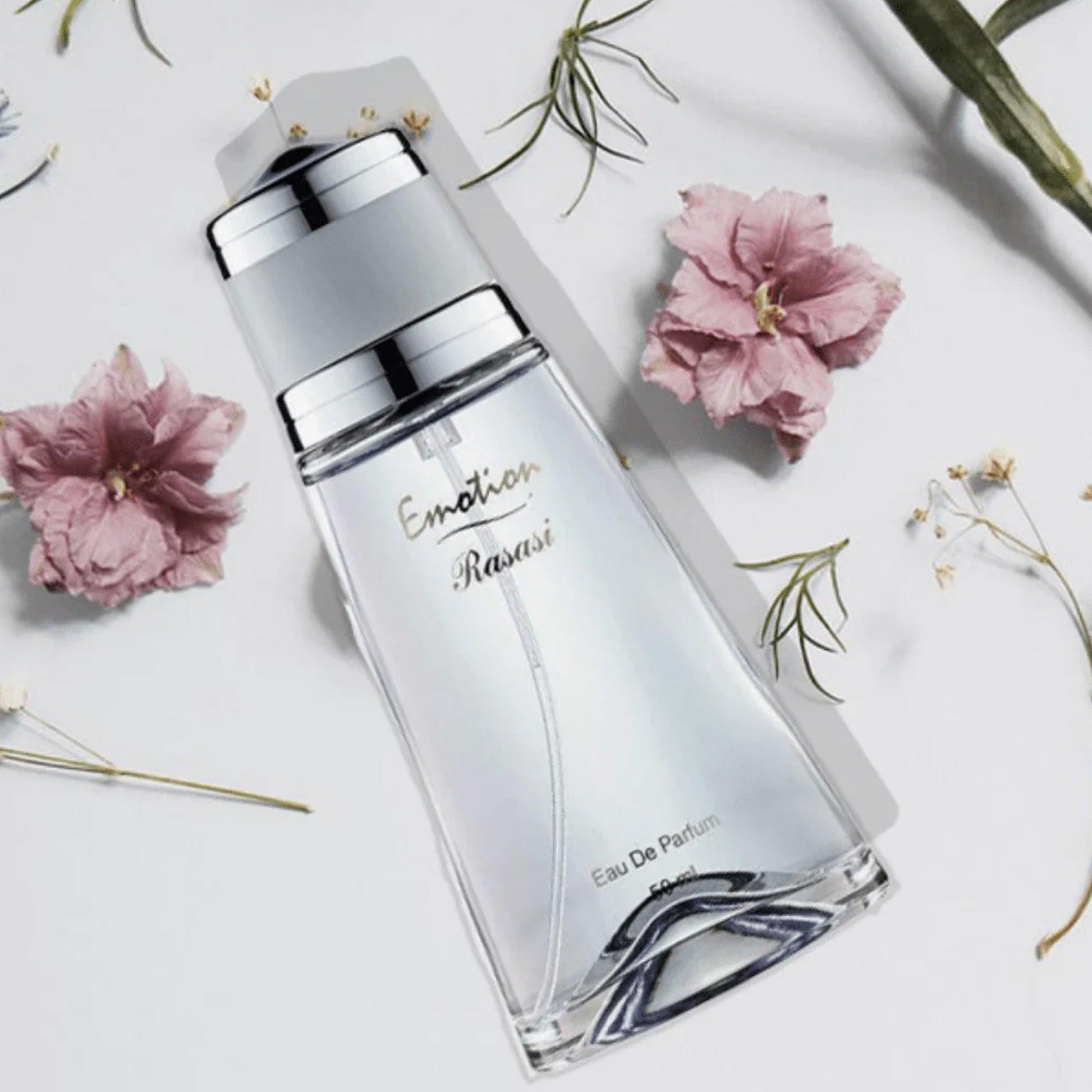 Rasasi Emotion Eau De Parfum bottle placed on a white surface decorated with soft pink flowers and green stems, creating a fresh and elegant look.