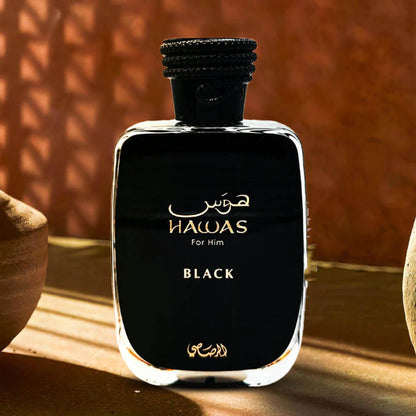Rasasi Hawas For Him Black perfume bottle in glossy black finish with gold lettering, placed in warm sunlight against an earthy brown background, reflecting a bold masculine fragrance style