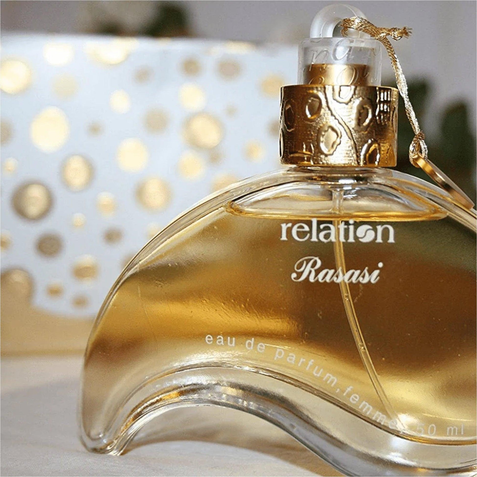 Rasasi Relation Eau De Parfum 50ml bottle with a curved golden design placed against a soft background featuring gold polka dot patterns.