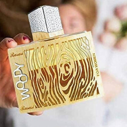 Rasasi Woody for Women Eau De Parfum bottle with a wood-grain inspired golden design held in hand against a soft blurred background.