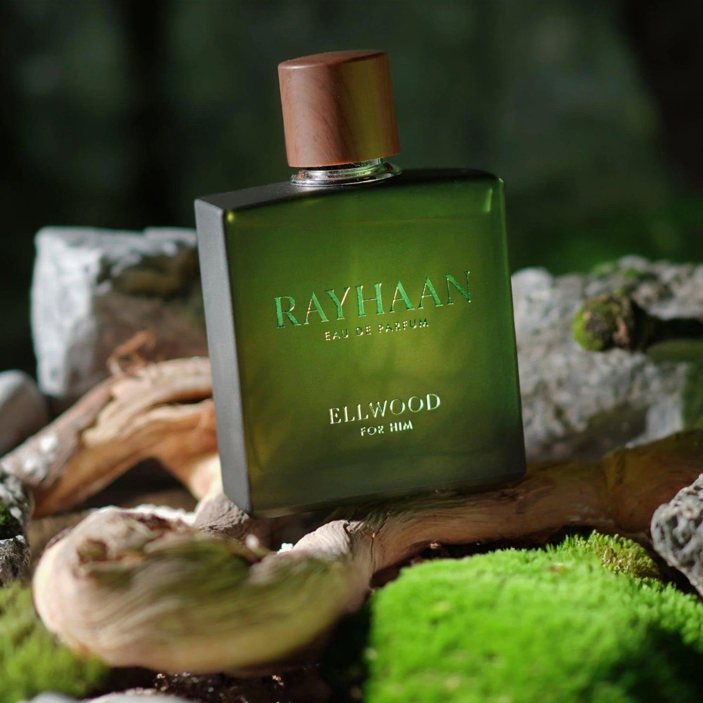 Rayhaan Ellwood For Him Eau De Parfum bottle in matte green glass with wooden cap placed on moss and tree bark in a natural forest setting