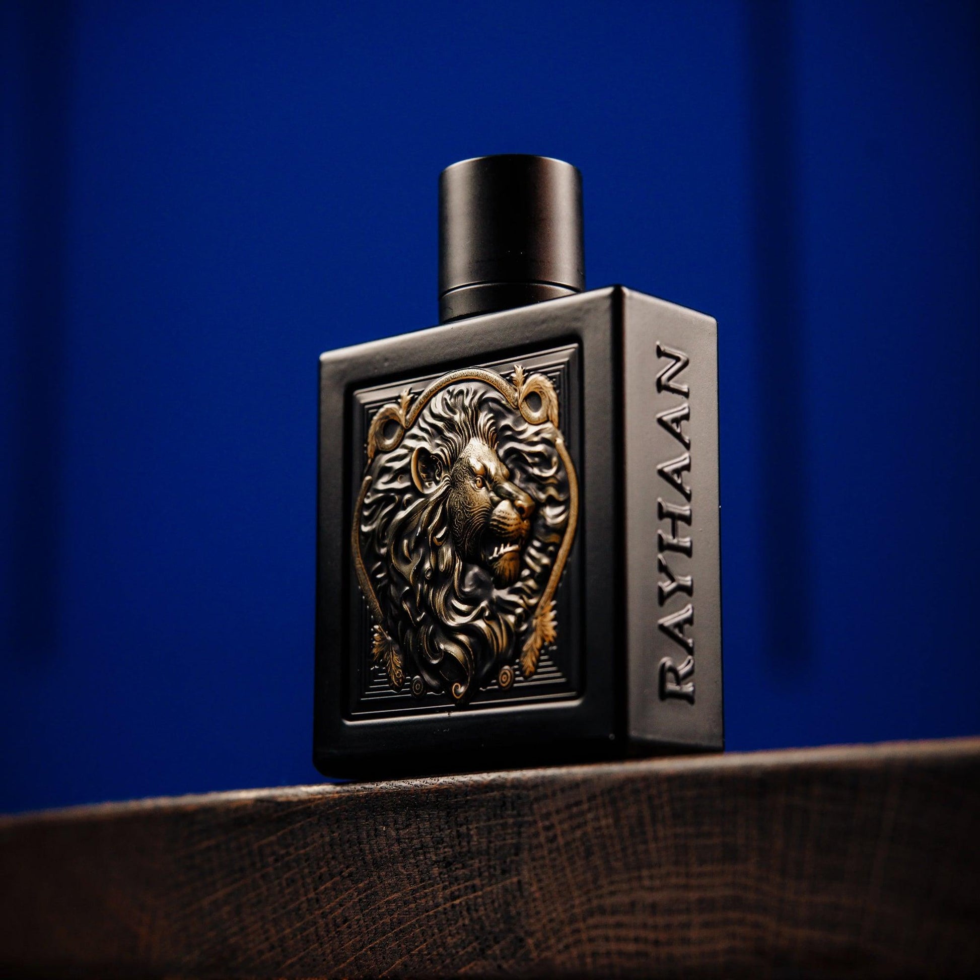 Rayhaan perfume bottle in matte black design featuring a golden lion emblem and embossed branding, placed on a wooden surface with a deep blue background
