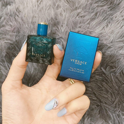 Hand holding Versace Eros mini perfume bottle and blue box on soft grey background