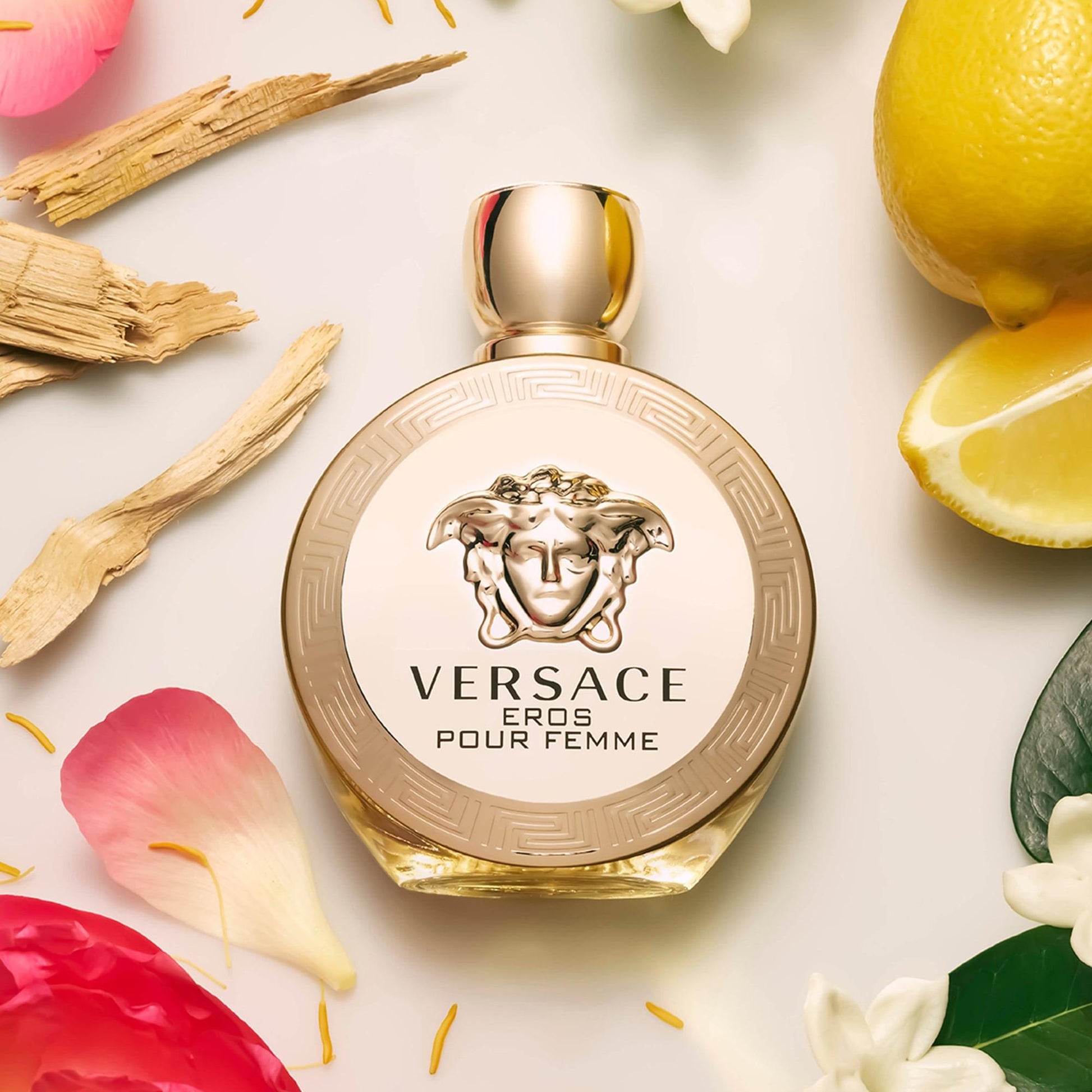 Versace Eros Pour Femme Perfume surrounded by petals and lemons on light surface
