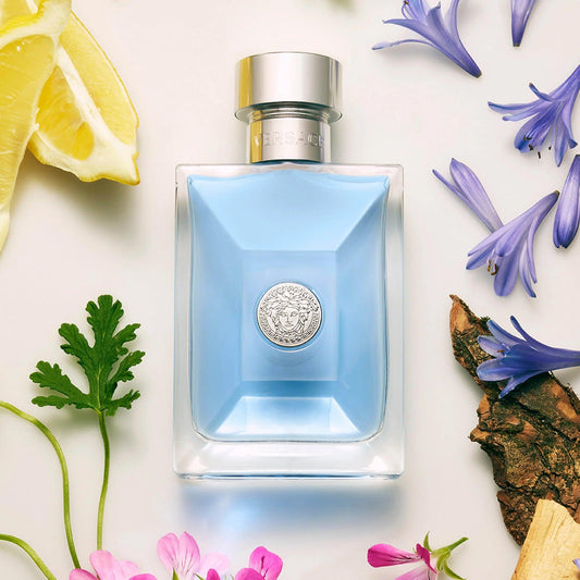 Versace Pour Homme Eau De Toilette bottle with light blue fragrance liquid placed among lemon slices, flowers, and woody notes on a white background