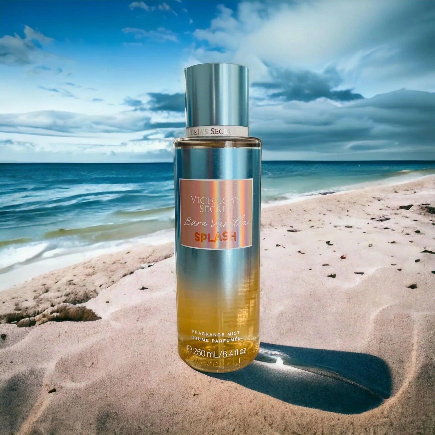 Victoria’s Secret Bare Vanilla Splash fragrance mist 250ml bottle placed on sandy beach with ocean waves and blue sky in the background