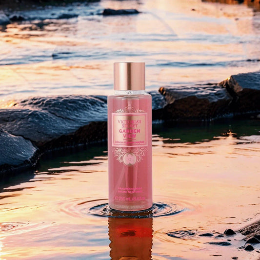 Victorias Secret Garden View fragrance mist 250ml bottle standing in shallow water during sunset with soft reflections and rocky shore background