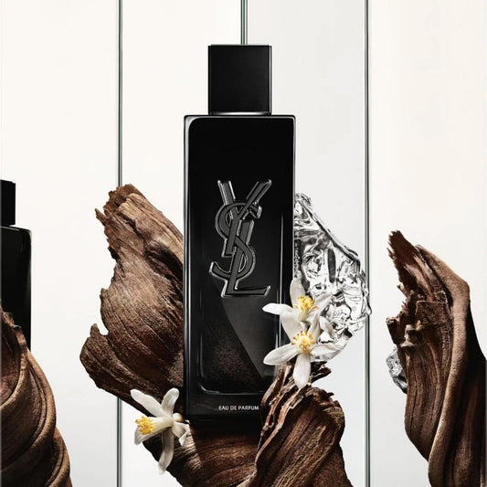 Yves Saint Laurent Y Eau De Parfum black bottle with YSL logo displayed among wood textures, ice, and white floral accents on a bright background